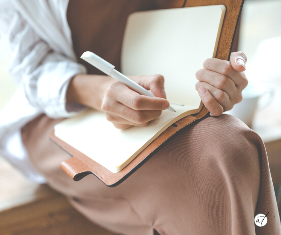 A photo of a woman with a notebook and pen preparing to journal just one of the amazing tools available via the mind archive on the andie thueson blog.