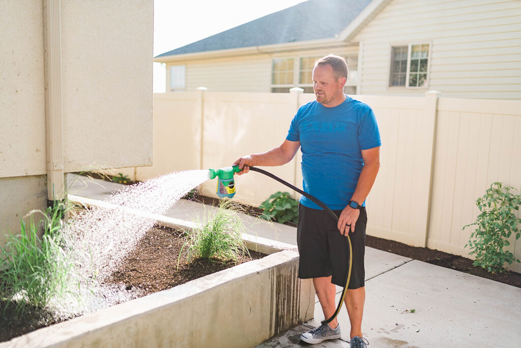 Photo of Kelly demonstrating the use of the Miracle Gro Sprayer connected to the hose 