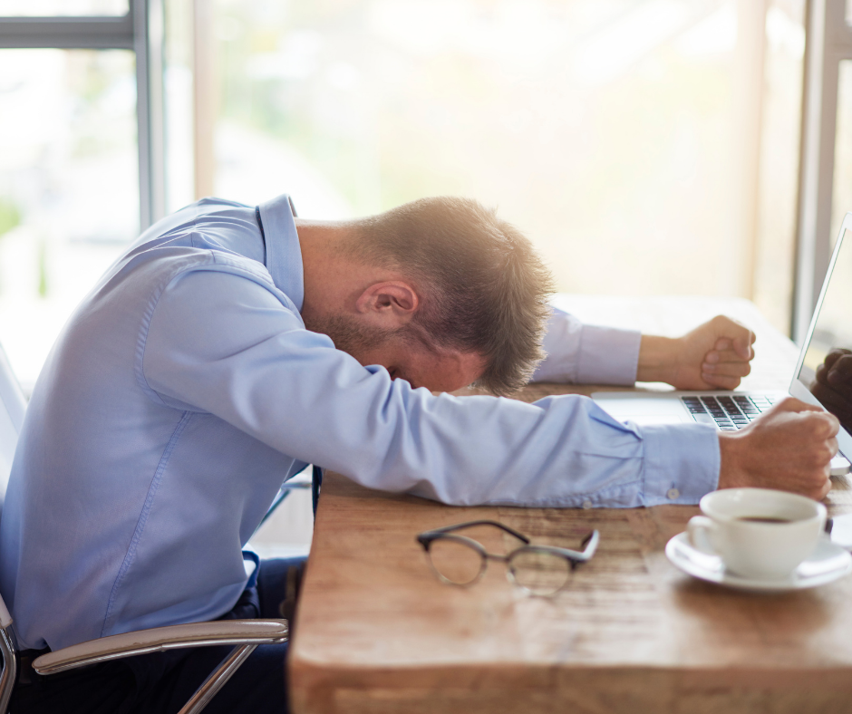 Photo of man in a blue shirt stressed and frustrated. His head is on the desk and his fists clenched. This is why men need space. To help process emotions. 