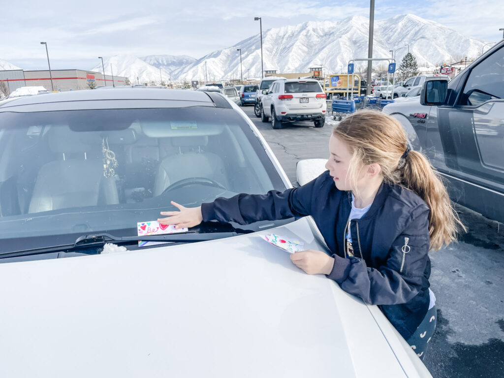 Photo of Andie's daughter placing the notes they made as part of the 30 day kindness challenge on someone's windshield. 
