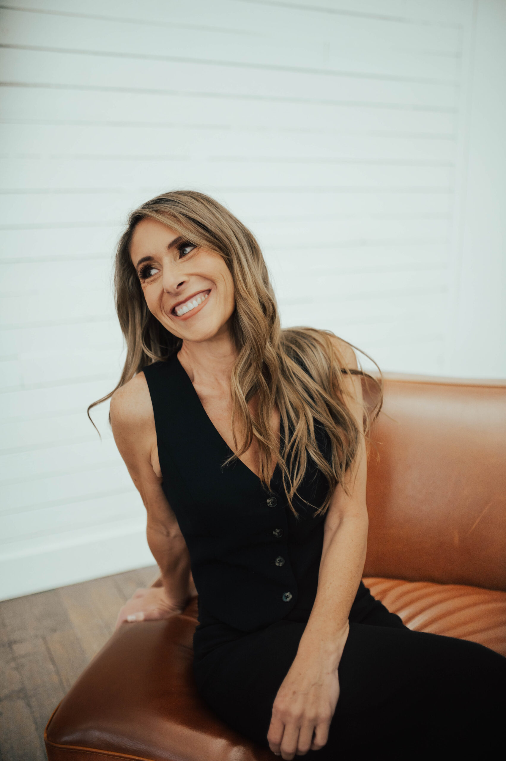 Andie Thueson, smiling while sitting on a brown leather chair.